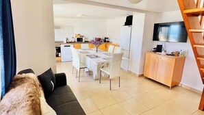 A modern living room with a sofa, a dining table with chairs, a kitchen area with appliances, and a TV mounted on the wall. - Escape to Tranquility in Estreito da Calheta, Portugal (Calheta)
