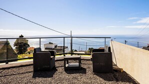 A terrace with two wicker chairs and a small table, overlooking a coastal view with buildings and a clear sky. - Escape to Tranquility in Estreito da Calheta, Portugal (Calheta)