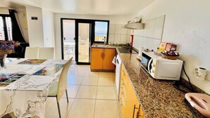 A modern kitchen with granite countertops, a microwave, and a sink. There is a dining area with a table and chairs, and a view of the outdoors through a sliding door. - Escape to Tranquility in Estreito da Calheta, Portugal (Calheta)