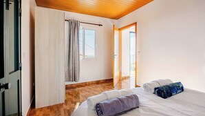 A hotel room with a wooden ceiling, a bed with white and purple towels, a window with curtains, and a wooden floor. - Escape to Tranquility in Estreito da Calheta, Portugal (Calheta)