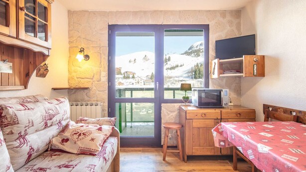 A cozy room with a sofa, a small wooden desk with a TV, and a view of a snowy mountain. - Cute studio apartment for 4 people, balcony and garage (Chamrousse)