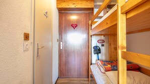 A narrow hallway leading to a wooden door with a heart-shaped decoration. A bunk bed with a colorful blanket is visible to the right. - Cute studio apartment for 4 people, balcony and garage (Chamrousse)
