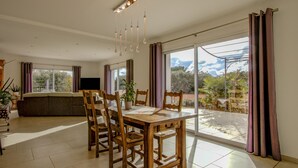 A dining area with a wooden table and chairs, a potted plant, and a large window with curtains. - Air-conditioned villa with private pool – Wheelchair accessible – Drôme Provençale (Saint-Restitut)
