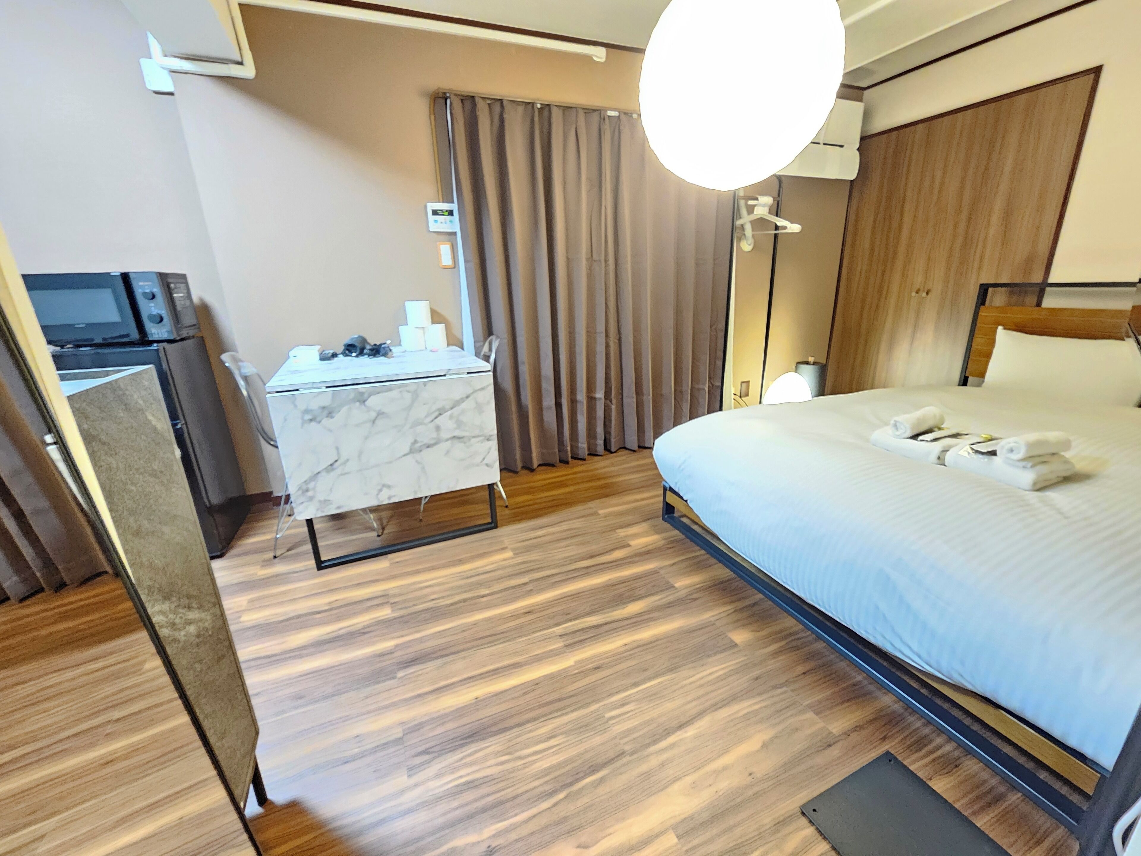 A hotel room with a bed, a desk with a computer, a TV, and a curtain.