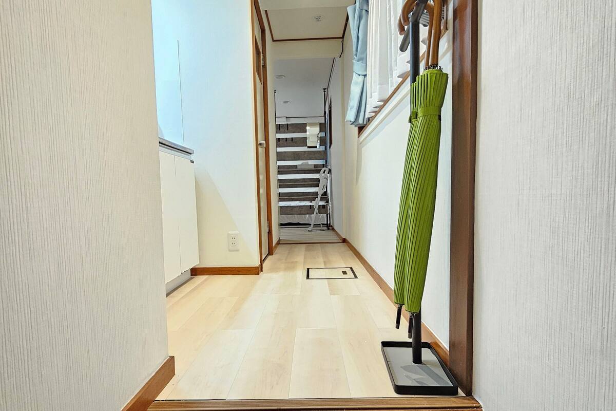 Un couloir étroit avec un plancher en bois, un parapluie vert posé sur un porte-parapluie et un escalier en arrière-plan.