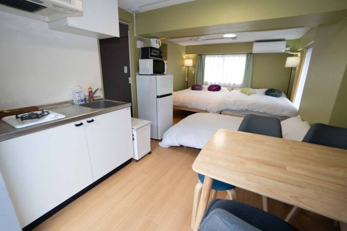 Une pièce compacte comprenant un coin cuisine, un lit avec des oreillers, une petite table et une chaise.