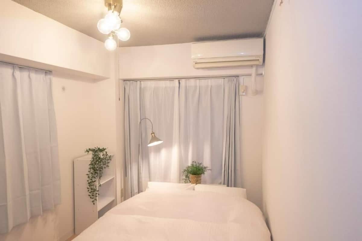 Une chambre à coucher avec un lit, une plante sur la table de chevet, une lampe et un appareil de climatisation.