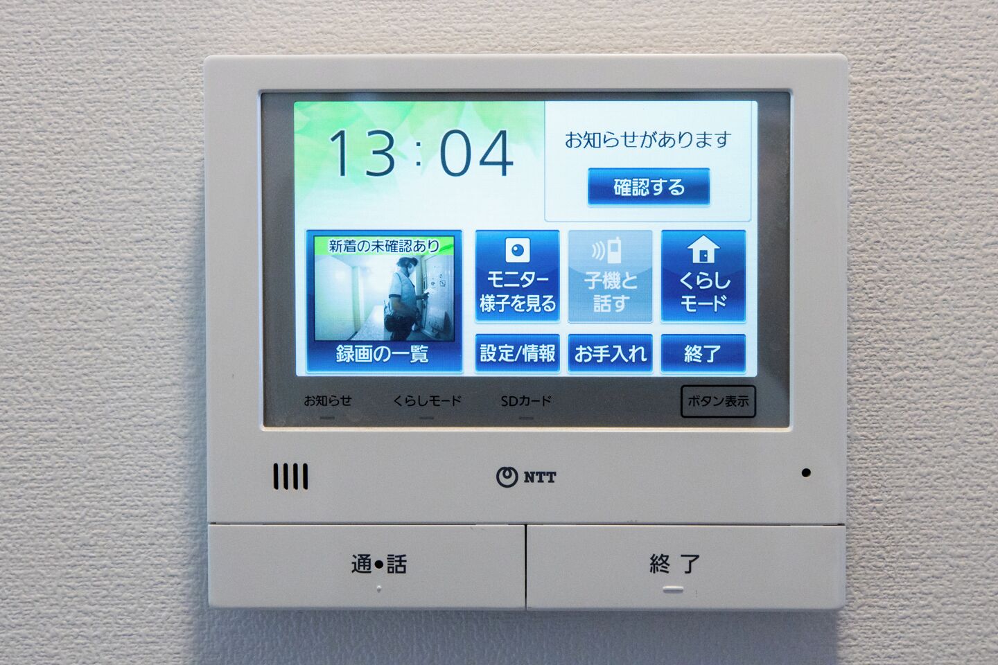 A digital display on a wall-mounted device with a time of 13:04, various menu options, and a logo labeled "NTT".