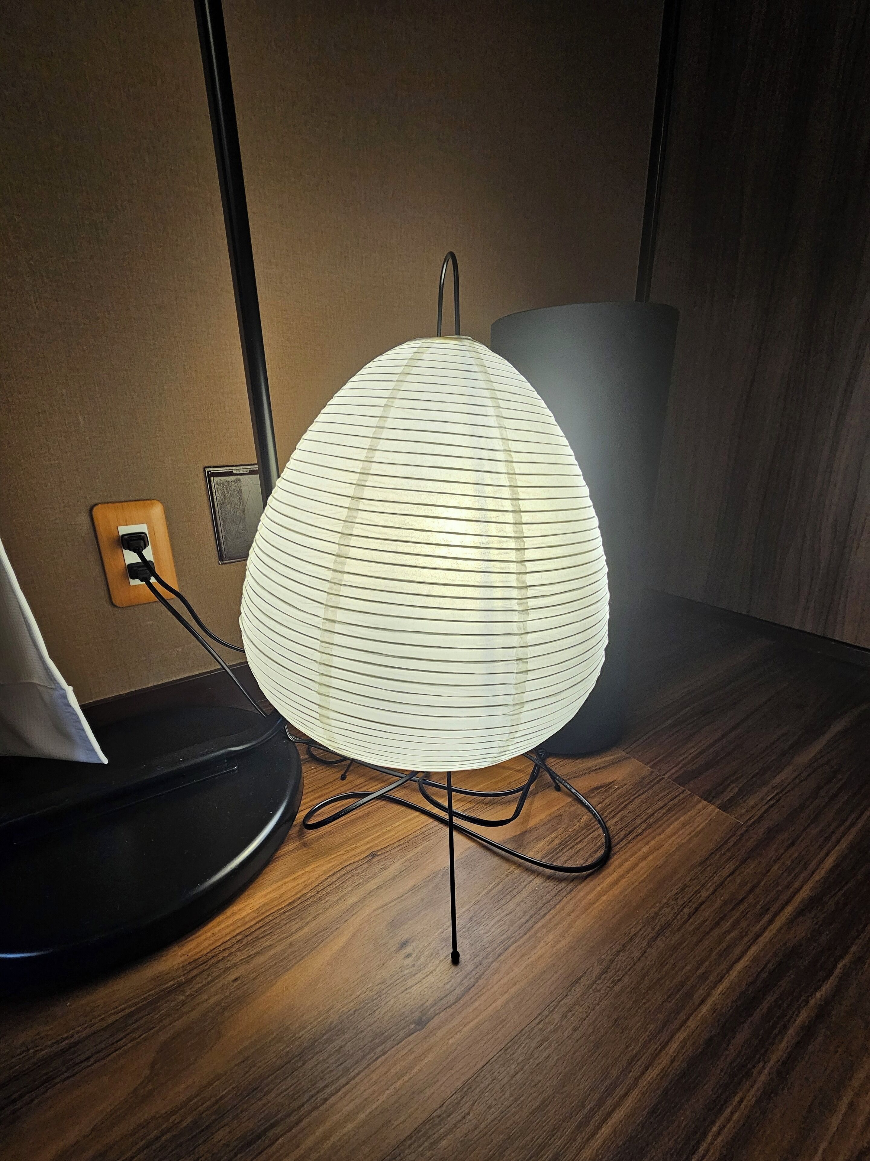 A modern lamp with a ribbed design on a wooden table, next to a laptop and a power outlet.