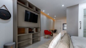 Ein modernes Wohnzimmer mit Flachbildfernseher, einem roten Sessel, einer Couch und einem kleinen Hocker.