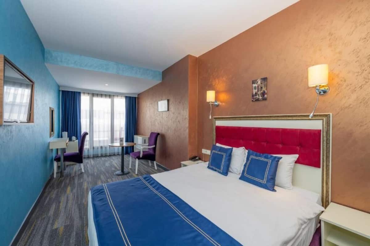 A hotel room with a large bed, a desk, and a chair.
