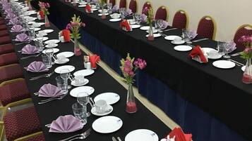 Una sala conferenze con un lungo tavolo apparecchiato per una riunione, completa di sedie, piatti, posate e centrotavola floreali.