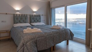 Ein modernes Schlafzimmer mit einem großen Bett, zwei Nachttischlampen und Blick auf eine verschneite Landschaft durch ein großes Fenster.