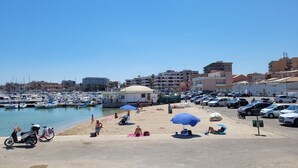 Ein Yachthafen mit Booten, einem Sandstrand und Gebäuden im Hintergrund.