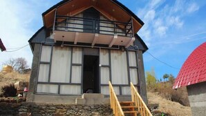 A two-story building with a balcony, a stone foundation, and a red roof. - The Ridge | Hill Top | Sainjh Valley - TrekNgo, Entire cottage in Sainj, India (Raila)