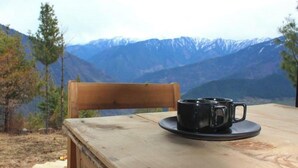 A wooden table with a black mug on a saucer, a wooden chair, and a mountainous landscape in the background. - The Ridge | Hill Top | Sainjh Valley - TrekNgo, Entire cottage in Sainj, India (Raila)