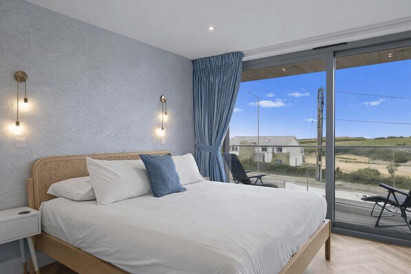 A bedroom with a large bed, a nightstand, a chair, and a view of the outside. - Modern Apartment with Balcony, Sea Views & Parking (Newquay)