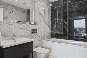 A modern bathroom with a marble vanity, a toilet, and a bathtub with a glass enclosure. - Modern Apartment with Balcony, Sea Views & Parking (Newquay)