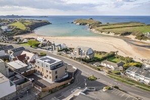 A coastal town with a sandy beach, a road leading to a roundabout, and residential buildings with visible driveways and parking spaces. - Modern Apartment with Balcony, Sea Views & Parking (Newquay)