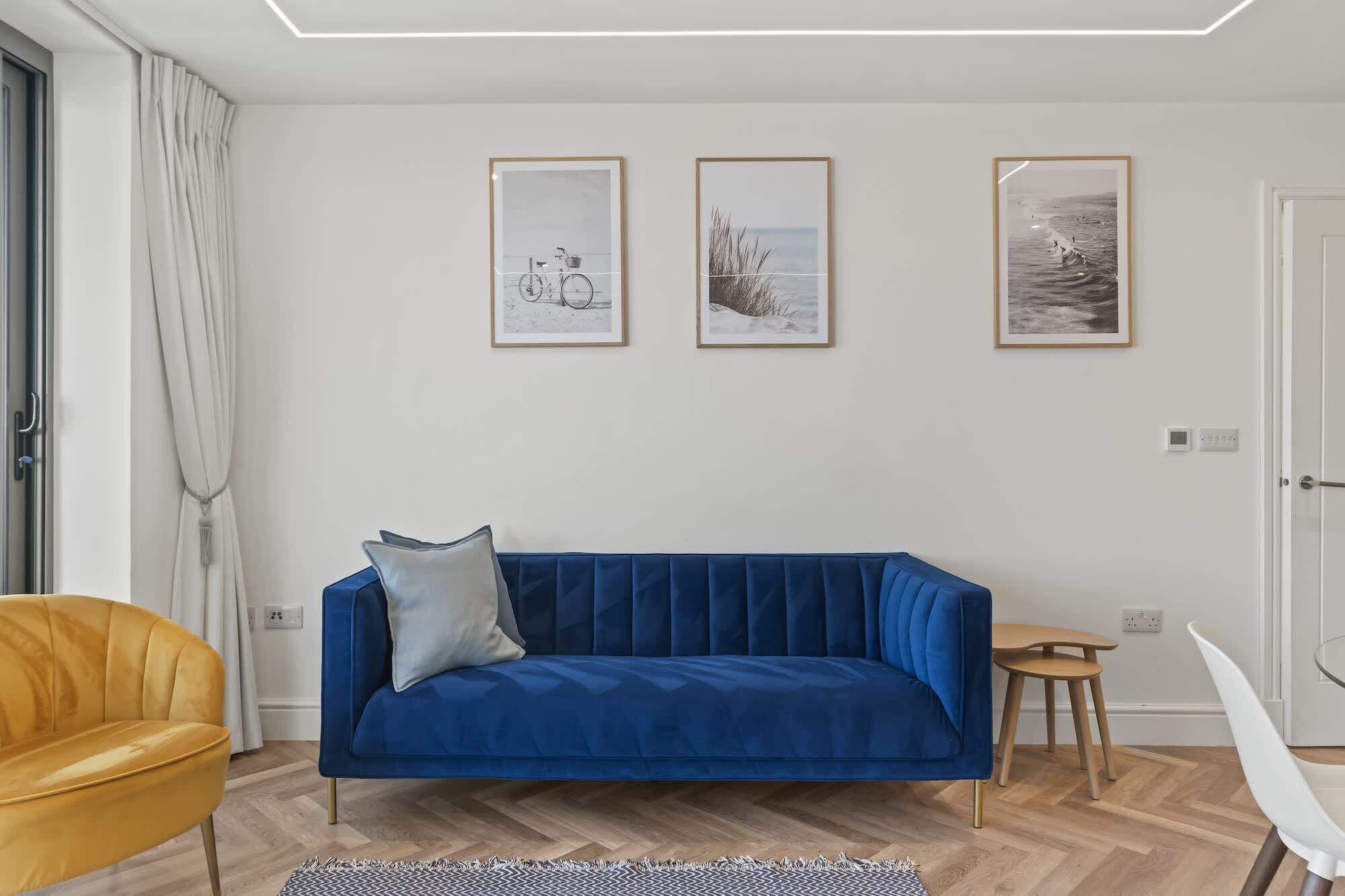 Una sala de estar moderna con un sofá azul, un sillón amarillo y un comedor con una mesa pequeña y sillas.