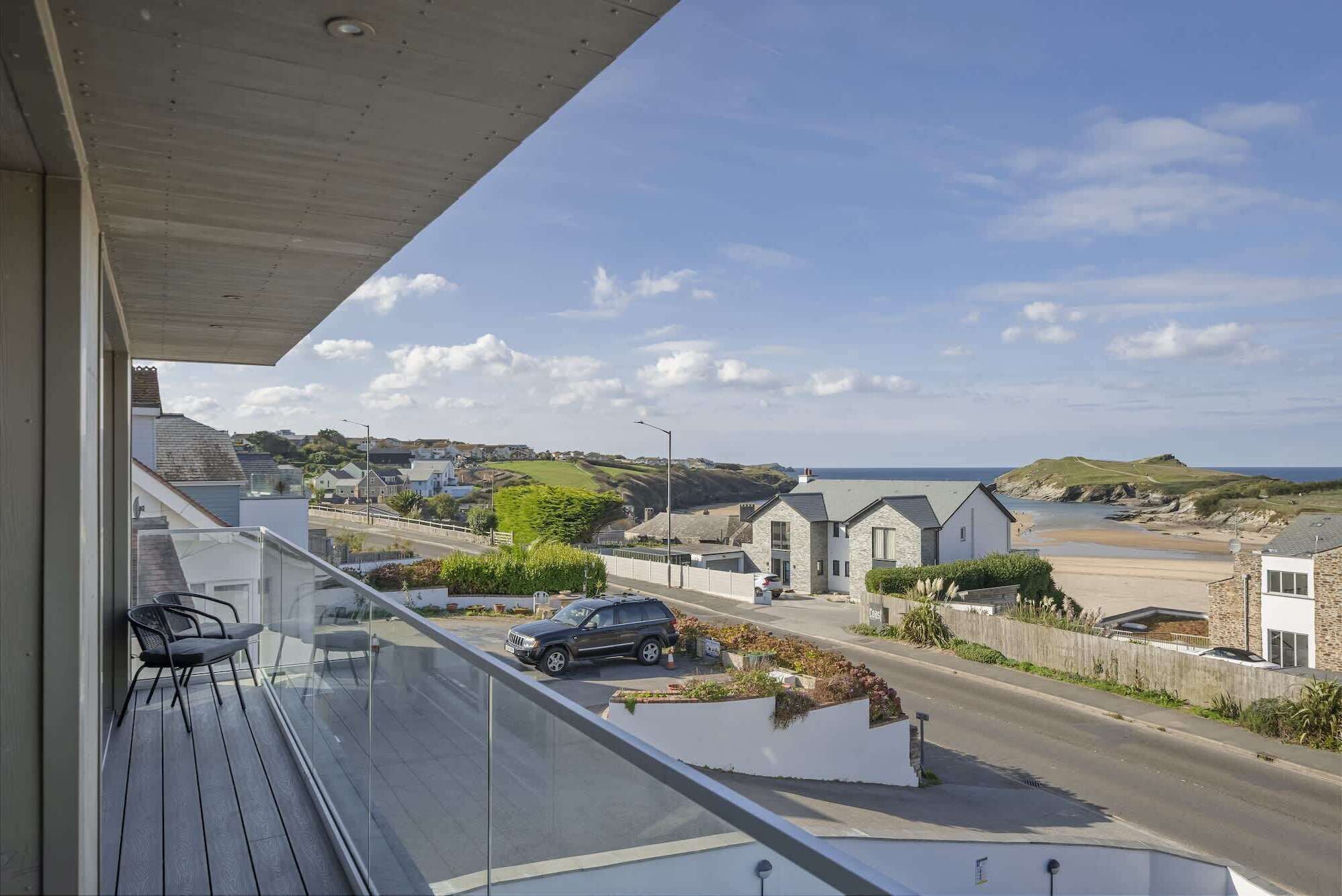A balcony with a clear view of a coastal road, houses, and the sea.