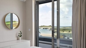 A bedroom with a large sliding glass door leading to a balcony with a view of the beach and cliffs. - Penthouse, Balcony with Expansive Sea Views, Parking (Newquay)