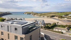 A coastal view with a modern building featuring large windows and a flat roof with solar panels. - Penthouse, Balcony with Expansive Sea Views, Parking (Newquay)