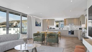 A modern apartment with a living area featuring a sofa, a dining table with chairs, and a kitchen with a marble countertop and an oven. - Penthouse, Balcony with Expansive Sea Views, Parking (Newquay)
