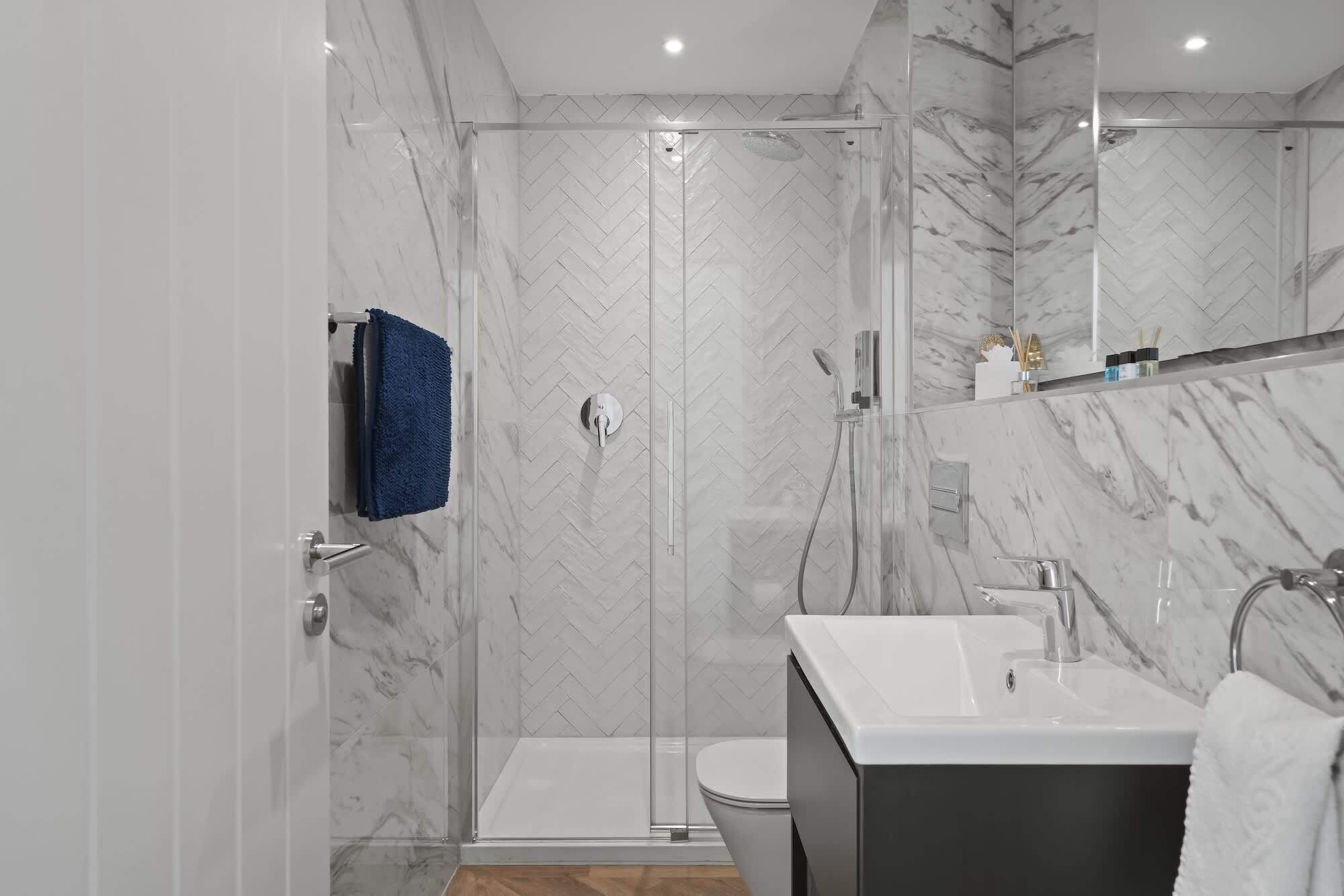 A modern bathroom with a glass-enclosed shower, a white sink, and a marble-tiled wall.