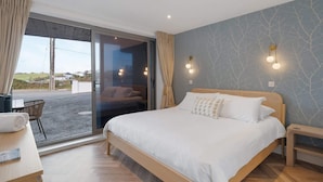 A bedroom with a large bed, a wooden nightstand, a desk with a chair, and a view through a sliding glass door to the outside. - Groundfloor Apartment, Easy Access Private Parking (Newquay)