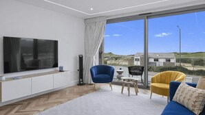 Una sala de estar moderna con un televisor de pantalla plana, un sofá, dos sillones, una mesa de centro y un amplio ventanal con vistas al campo.