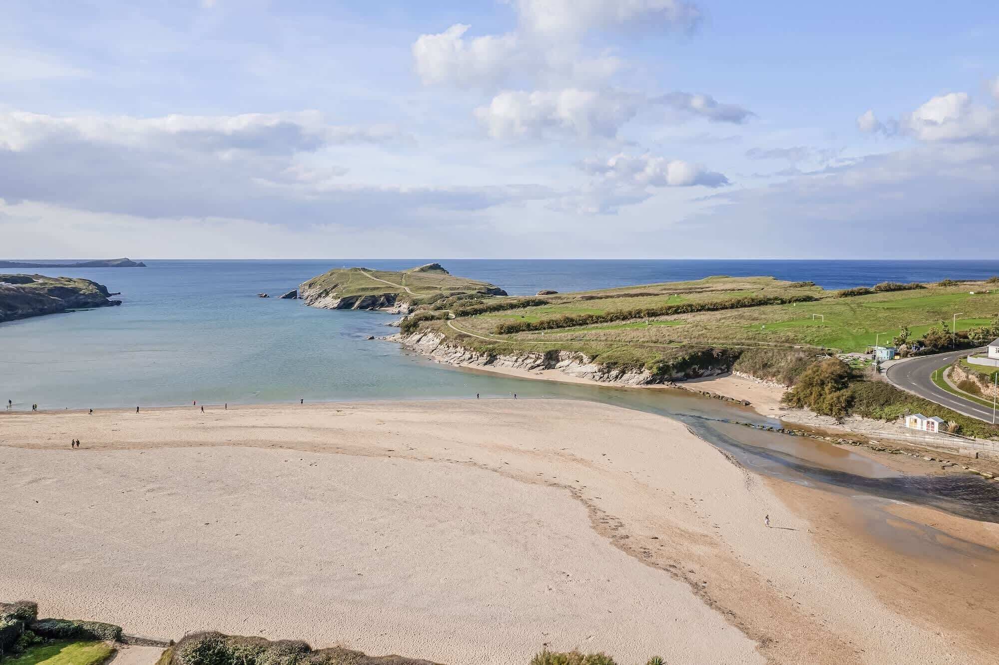 A coastal landscape with a sandy beach, grassy areas, and a road curving along the coast.