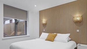 Un dormitorio moderno con una cama grande, una ventana con persianas y dos lámparas de pared.