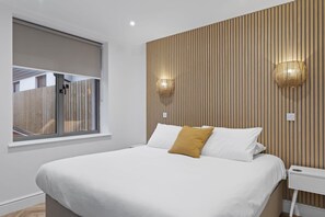 A modern bedroom with a large bed, a window with blinds, and two wall-mounted lamps.