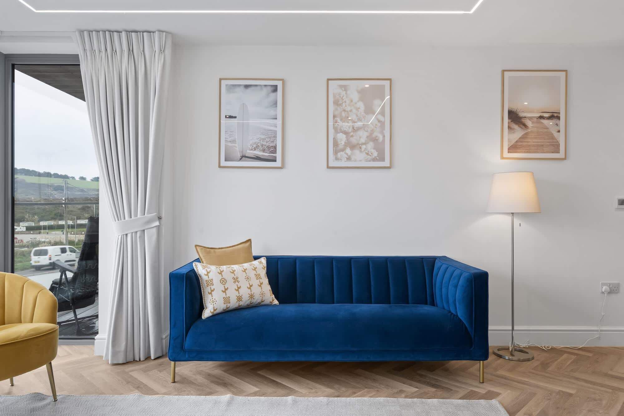 Una sala de estar moderna con un sofá azul, un sillón amarillo y una lámpara de pie. Hay tres cuadros en la pared.