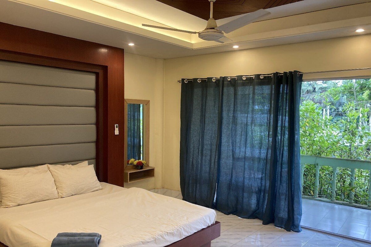 Un dormitorio con cama, ventilador de techo, ventana con cortinas y balcón con barandilla.