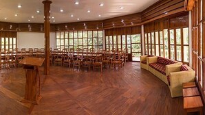 Ein geräumiger Saal mit Holzböden, Reihen von Stühlen, einer Couch und großen Fenstern.