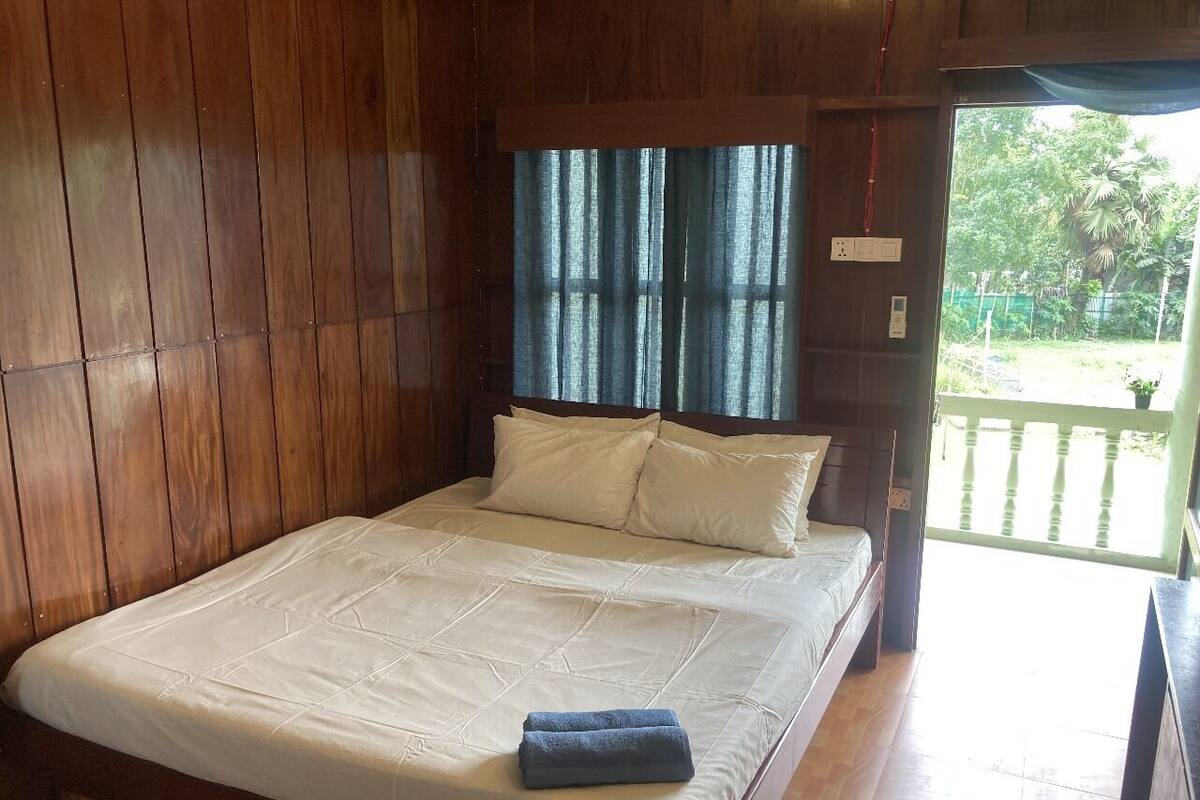 Una habitación con paneles de madera, una cama, una ventana con cortinas y vistas a zonas verdes.