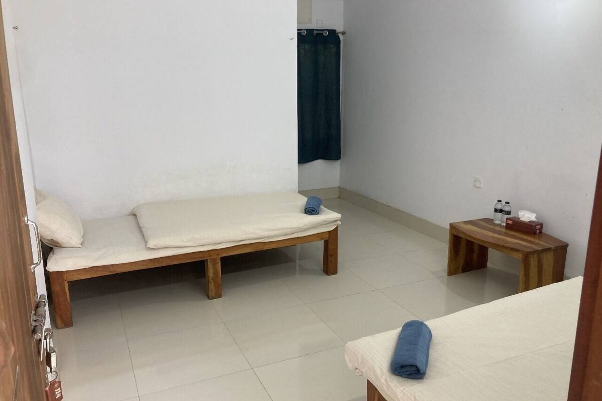 Una habitación con dos camas de madera, una pequeña mesa de madera con botellas y una cortina azul.