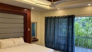 Ein Schlafzimmer mit Bett, Deckenventilator, Fenster mit Vorhängen und Blick auf Grünfläche.