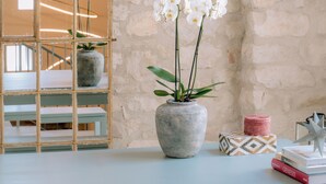 A room with a stone wall, a wooden-framed mirror, a table with a vase of white orchids, and hanging pink pendant lights. - Can Terrades by Artu (Beuda)