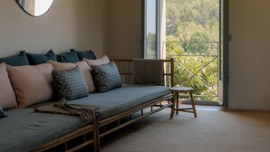 A room with a low wooden bed, a small chair, a large mirror, and a balcony with a view of trees. - Can Terrades by Artu (Beuda)