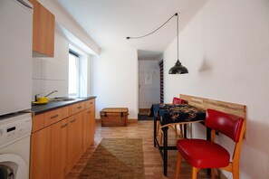 Una cocina compacta con armarios de madera, lavadora, comedor con mesa y sillas, y una lámpara colgante.