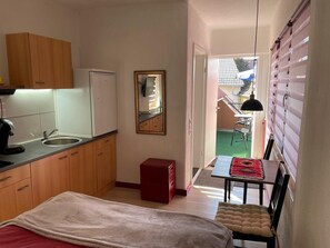 Cocina compacta con lavamanos, un refrigerador pequeño, armarios de madera, un armario rojo, un espejo y un comedor con mesa y silla.