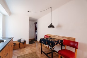 Una habitación con una mesa de comedor, sillas, una lámpara colgante, una cesta de mimbre y un armario de madera.