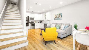 A modern apartment with a staircase leading to a kitchen, a living area with a sofa and a yellow armchair, and a dining area with a table and chairs. - 3 Bedrooms | Downtown Pensacola | Walkable Location | Fenced Yard (Pensacola)
