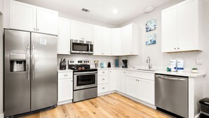 A modern kitchen with white cabinets, stainless steel appliances, and a wooden floor. - 3 Bedrooms | Downtown Pensacola | Walkable Location | Fenced Yard (Pensacola)