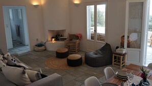 Ein modernes Wohnzimmer mit einer Couch, Hocker, einem Esstisch für zwei Personen und einem Kamin.