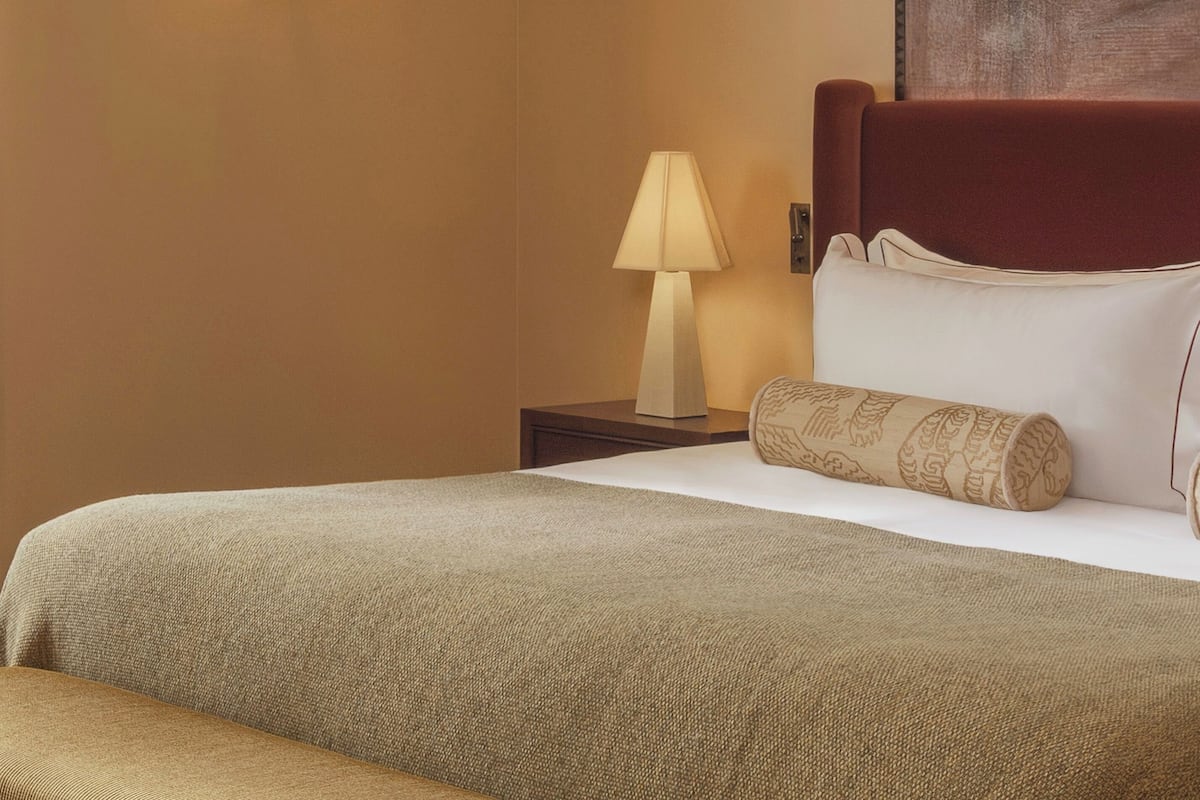 A hotel room with a bed, a nightstand, a lamp, and a pillow.