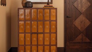 A wooden cabinet with floral designs, a framed abstract painting, and a patterned rug in a hallway.
